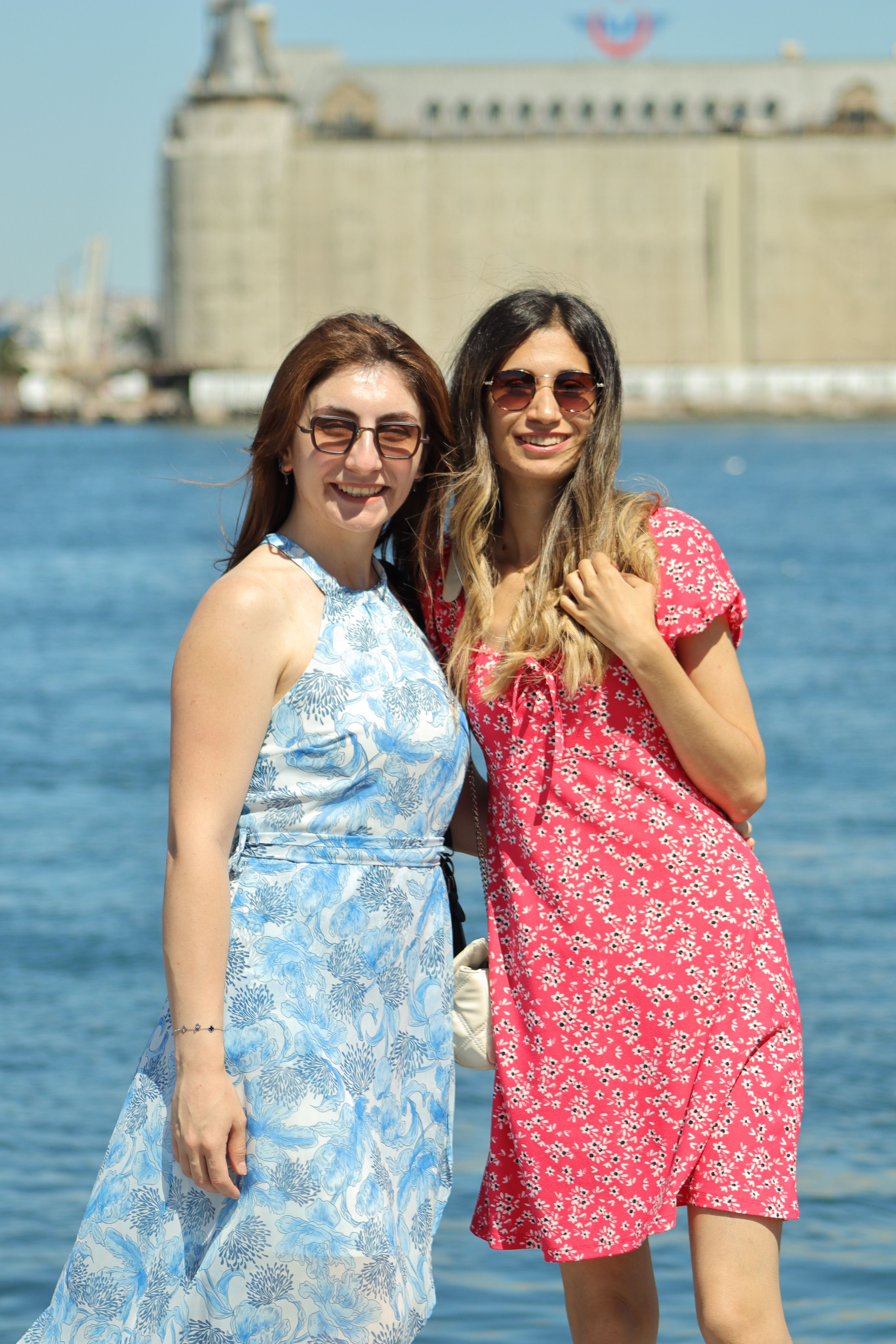 Two women enjoying the sunny day by the water, showcasing summer fashion and friendship.
