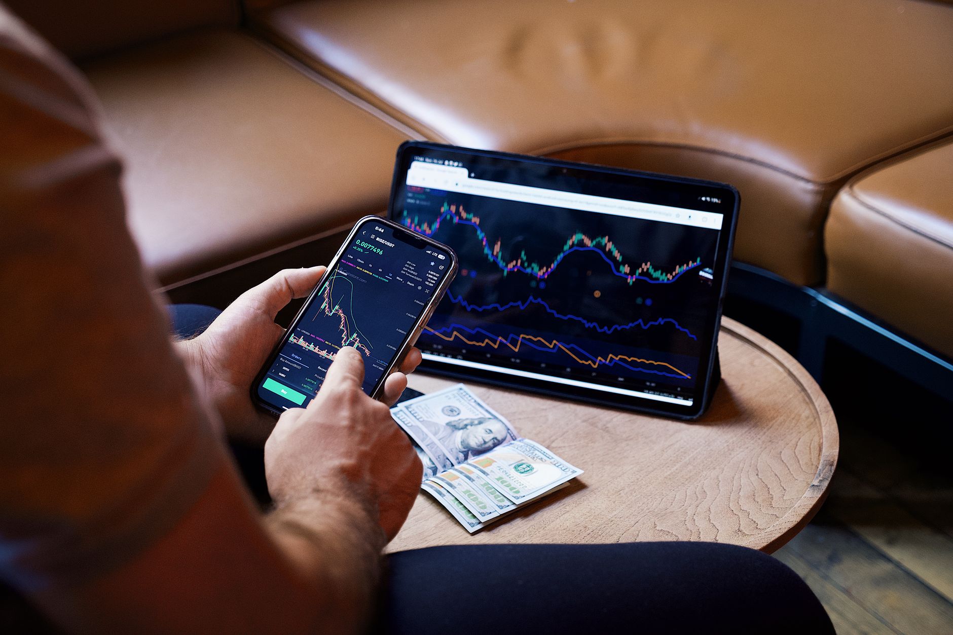 A person using a smartphone and tablet for stock market analysis, with graphs and cash visible — how do you make money from investing