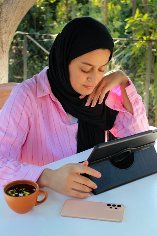 Free Young Woman Sitting at the Table and Using a Tablet  Stock Photo