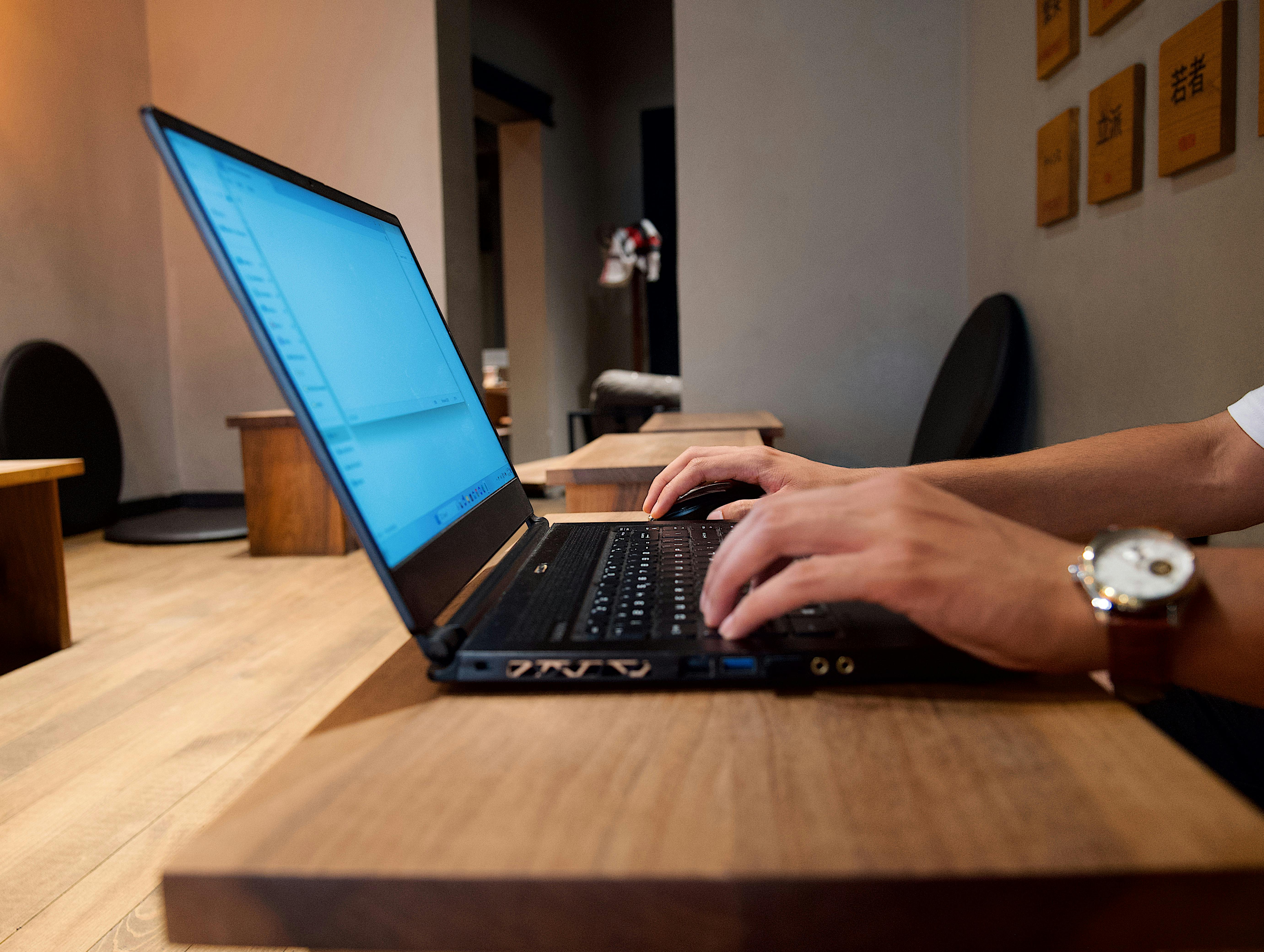 Hands typing on a laptop in a modern coffee shop, emphasizing remote work flexibility.