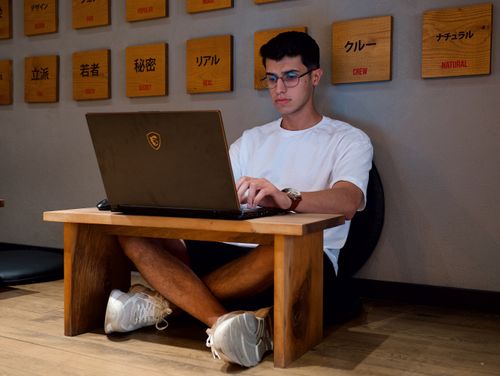 Free Young adult working remotely with a laptop while sitting cross-legged indoors. Stock Photo