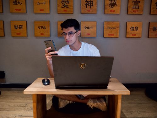 Free A young man using his smartphone and laptop for remote work indoors. Stock Photo
