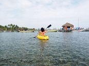 Woman kayaking in a yellow kayak on a tropical lake with pier and palm trees in view.