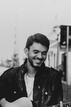 Young musician in a leather jacket smiling while playing guitar.