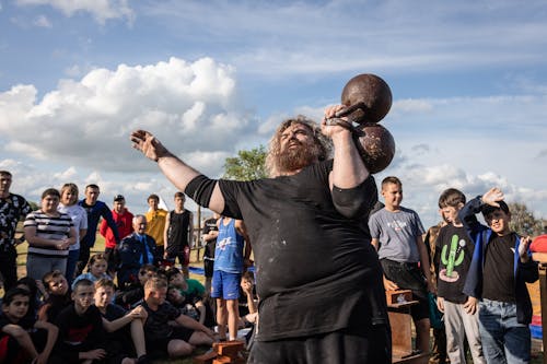 People Watching a Bearded Man Lifting Dumbbells at a Sports Contest