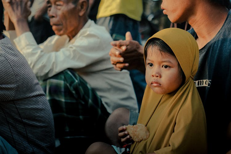 A Baby Sitting With Their Parent In The Crowd 