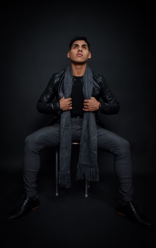 Free Portrait of a fashionable male model sitting in studio wearing a black leather jacket and scarf. Stock Photo