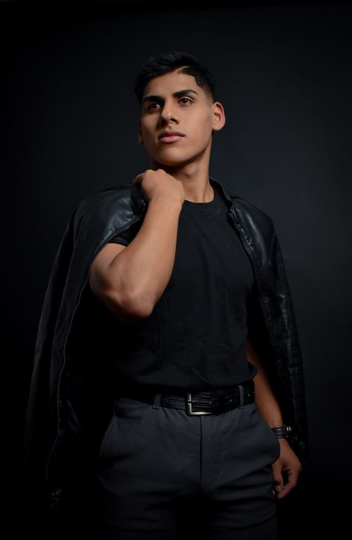 Free Confident male model poses in a black leather jacket against a dark studio backdrop. Stock Photo