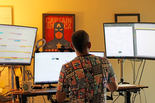 Back View of a Man Sitting at a Desk with Three Computer Monitors 