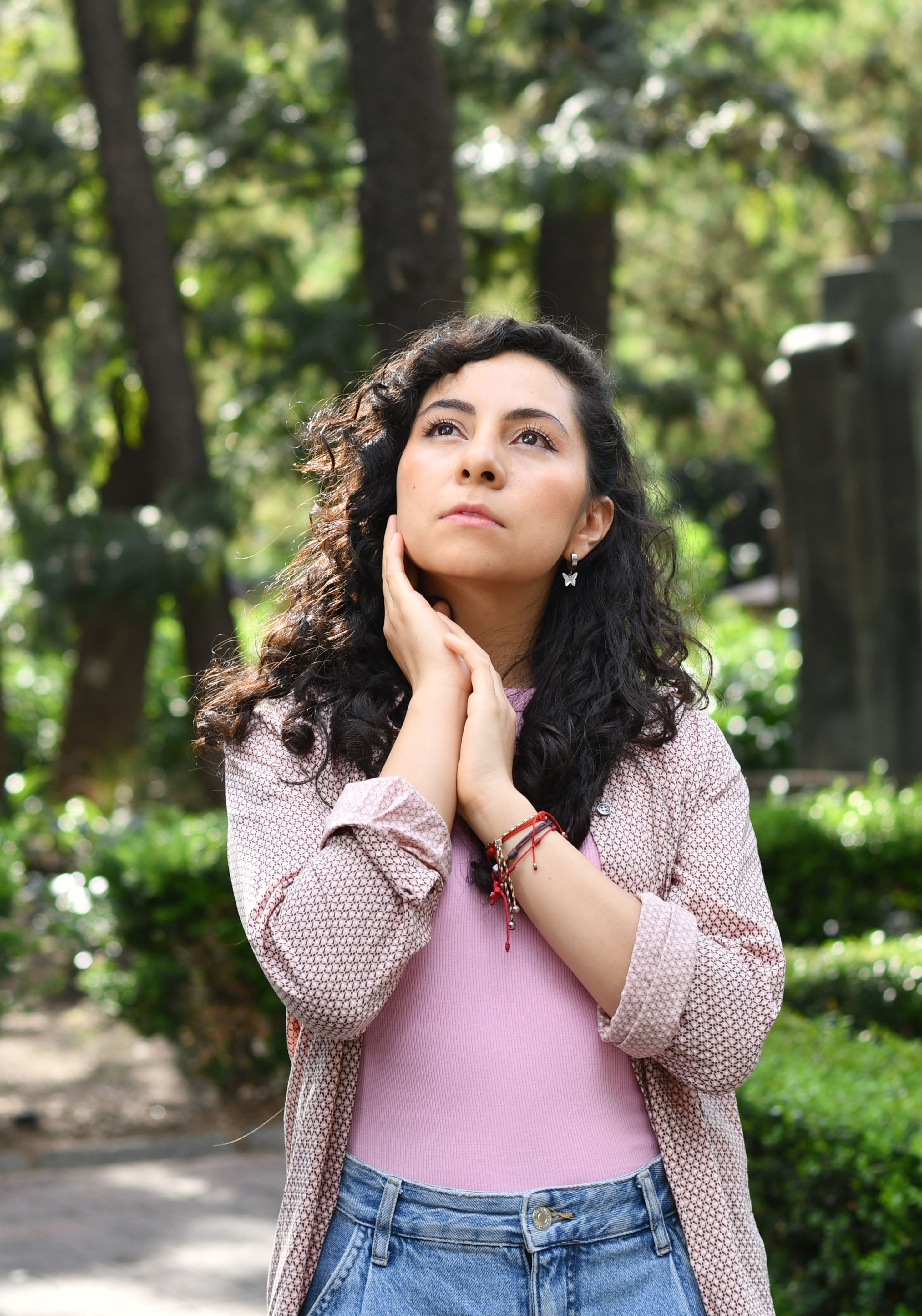 A young woman with curly hair looking contemplative in a sunny park in Mexico City.