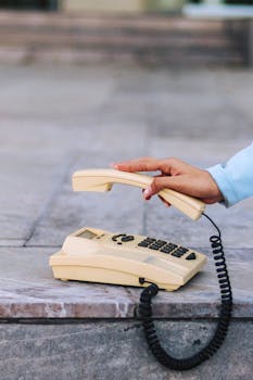 Close-up of a hand holding the receiver of a vintage landline phone on a stone surface.