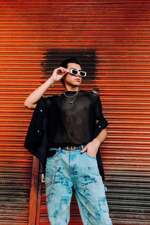 Free Stylish model in mesh top and sunglasses posing confidently by a rustic backdrop. Stock Photo