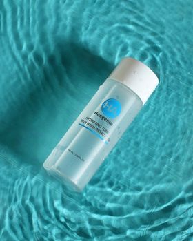 Floating hydrating face toner bottle on turquoise water with ripples, skincare theme.