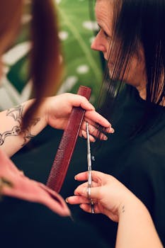 Hairdresser cuts woman's hair using scissors and comb in salon.