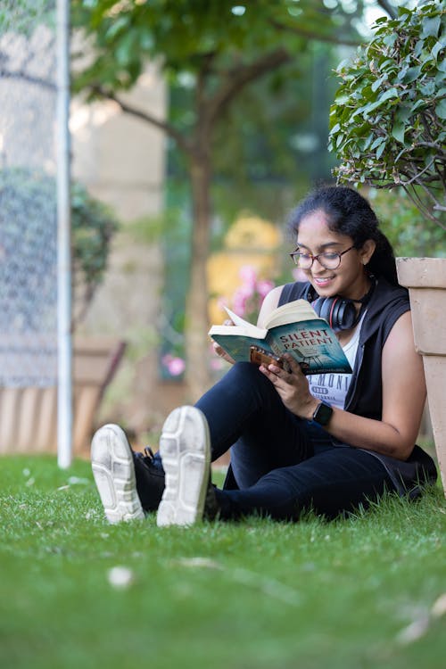 A Girl Sitting on the Grass in a Park and Reading a Book 