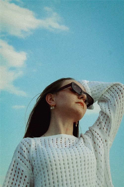 Free Low angle shot of a stylish woman in a sweater and sunglasses against a clear sky. Stock Photo
