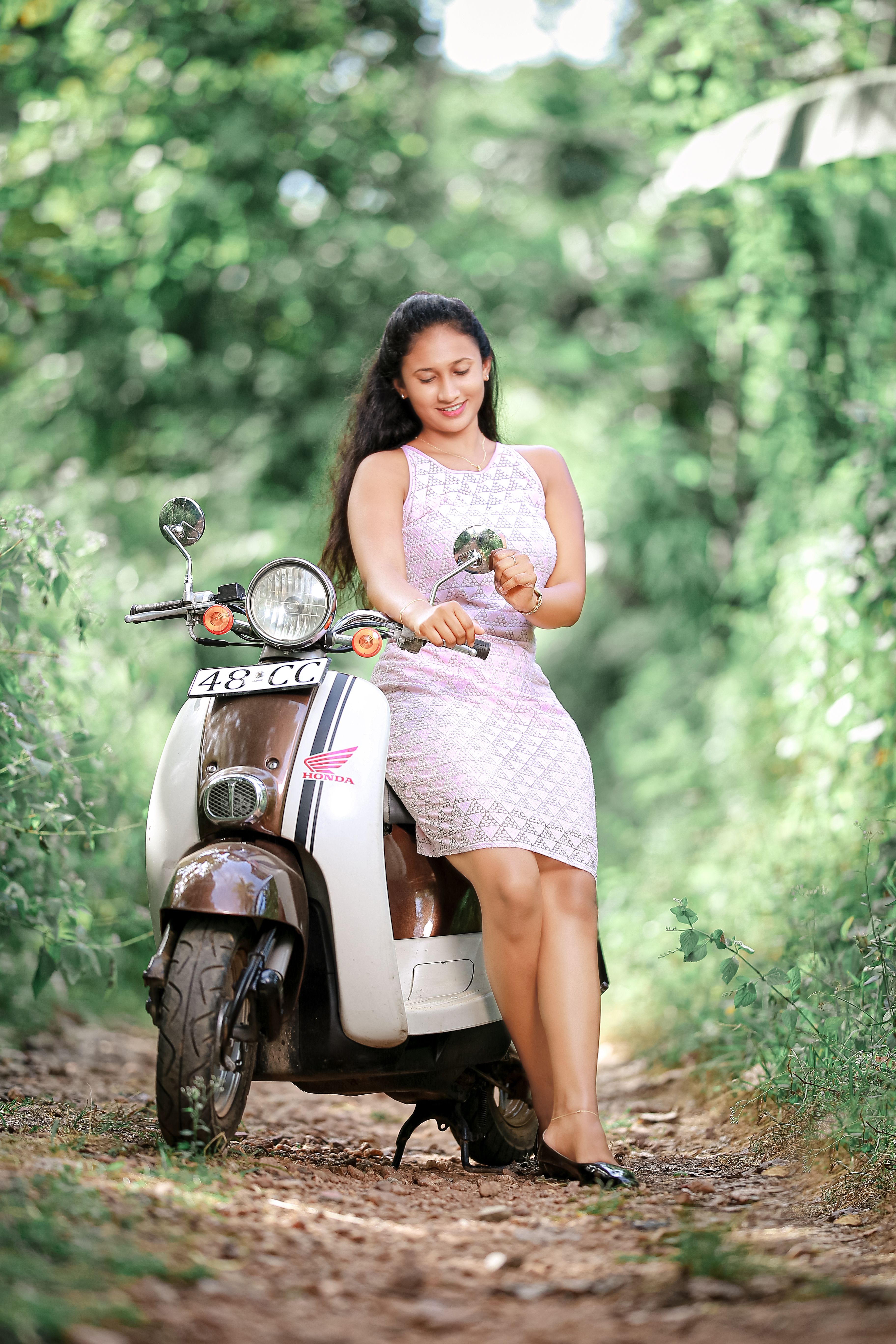 Woman sitting on a scooter in a scenic path surrounded by greenery, embodying relaxation.