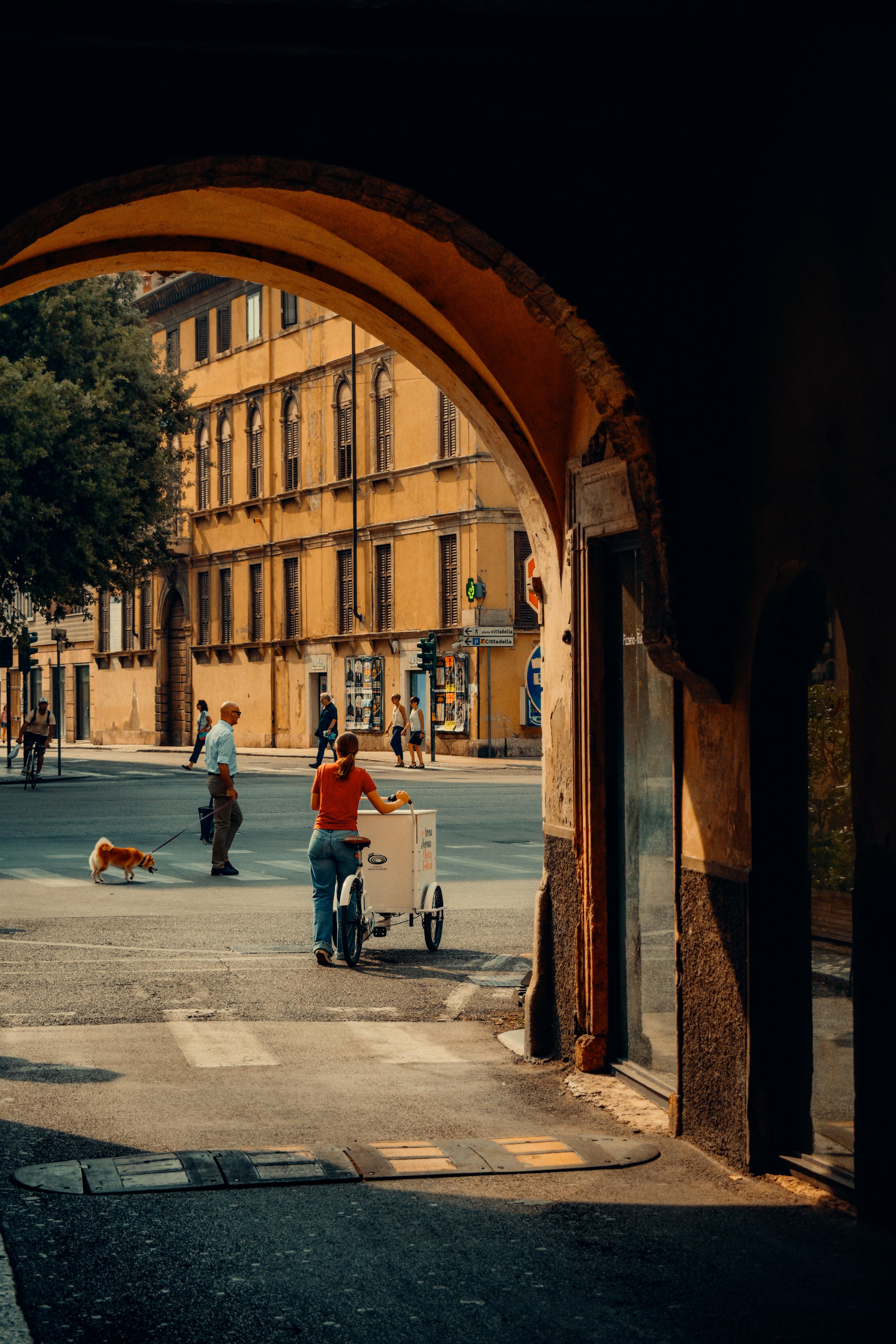 A summer day in Verona, Italy, with pedestrians and classic architecture seen through an archway.