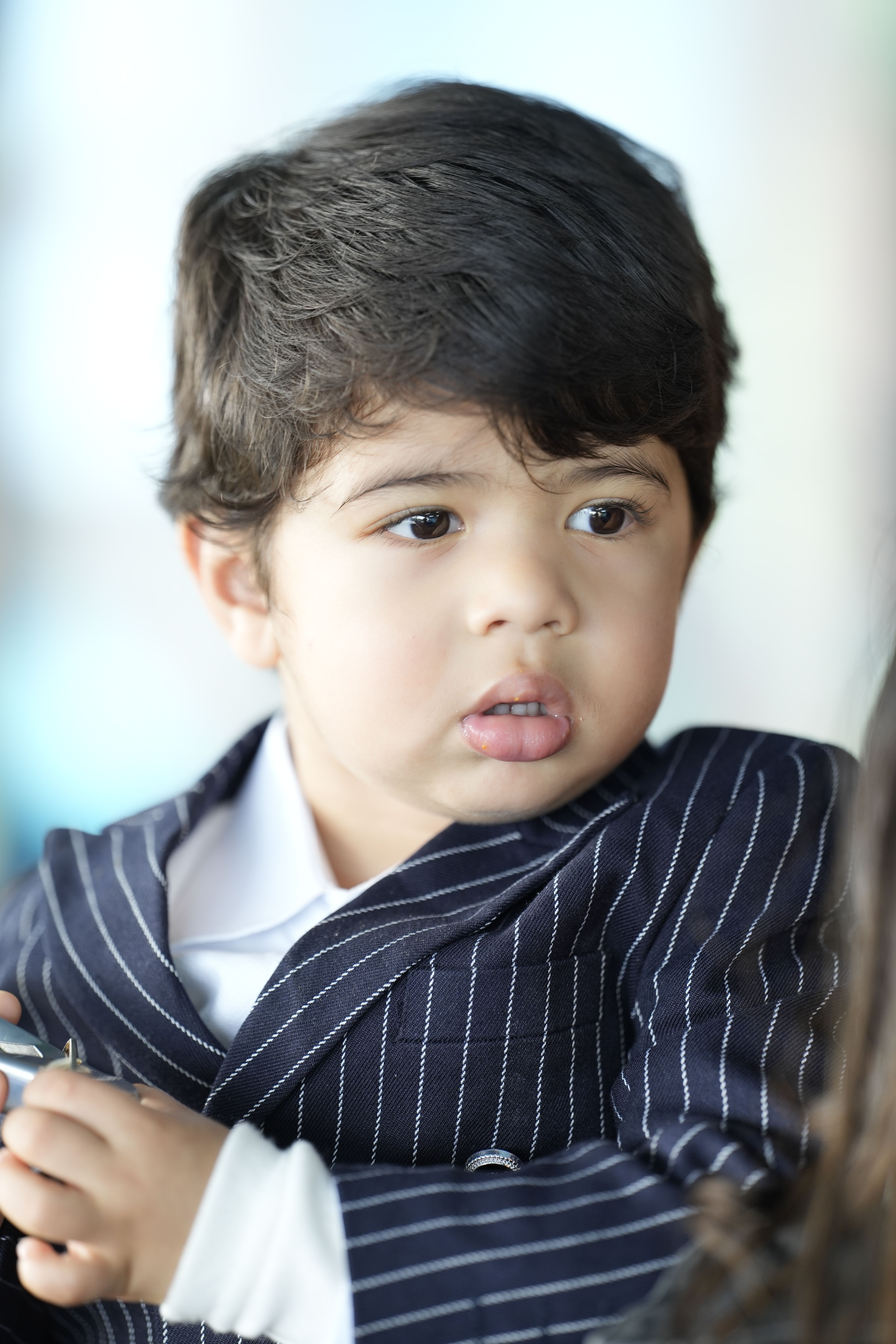 A young child in a pinstripe suit looks attentively at something off-camera.