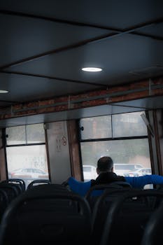 Man sitting alone on a public transport bus, back view, traveling in daytime.