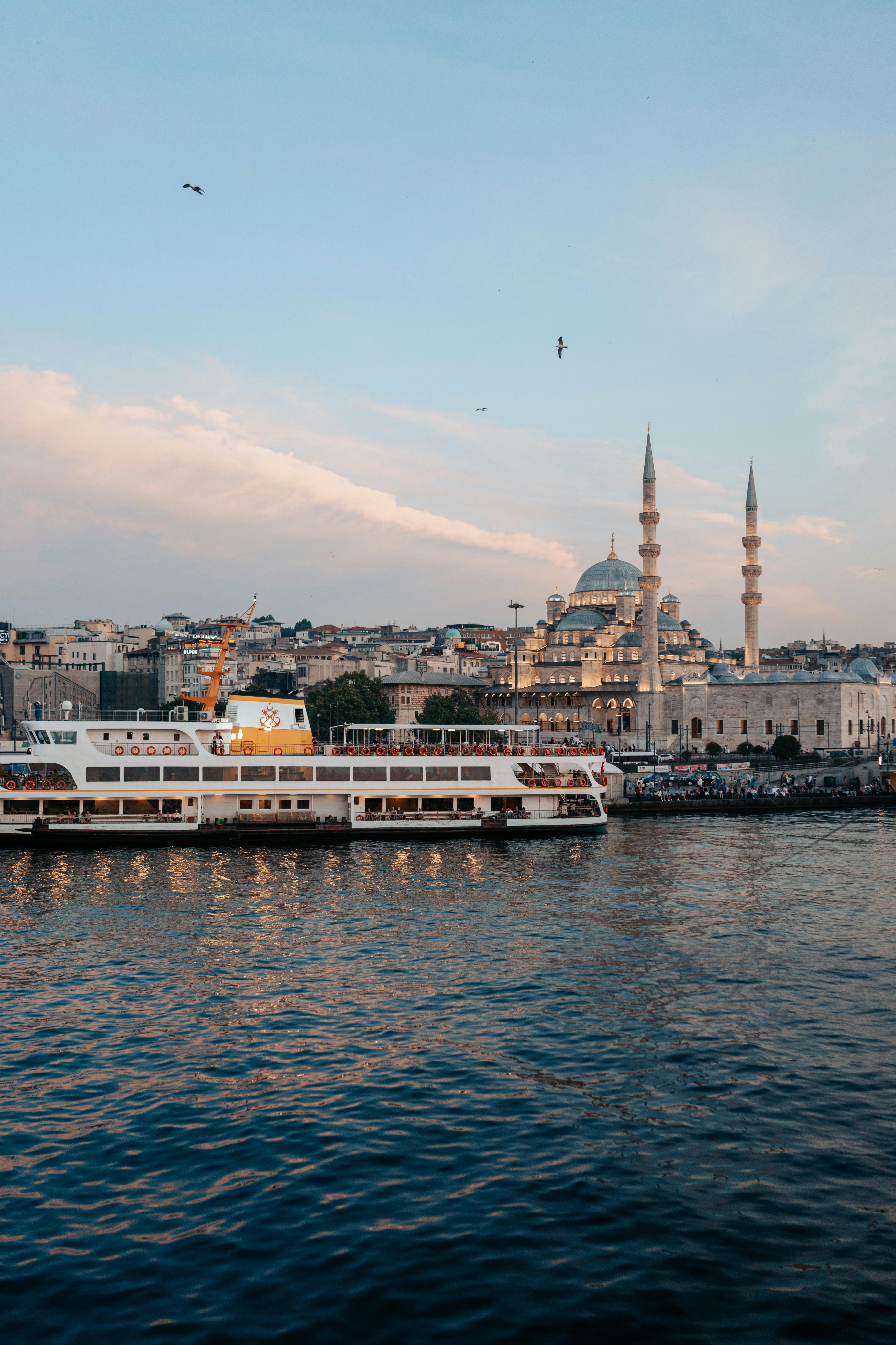 Scenic view of a ferry crossing the Bosphorus with Istanbul skyline and mosque at sunset.