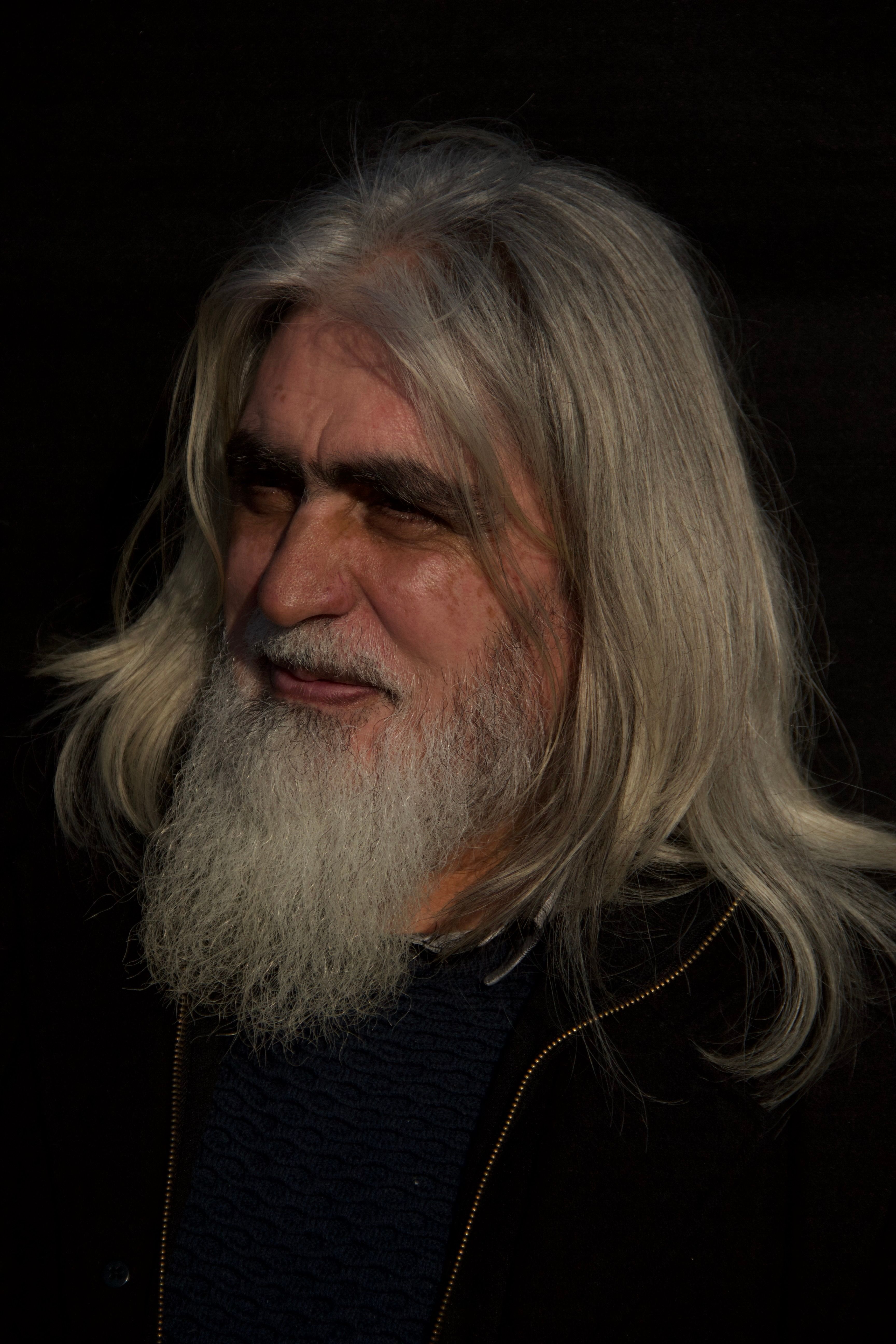 Close-up of a senior man with a long beard and gray hair, showcasing a contemplative expression.
