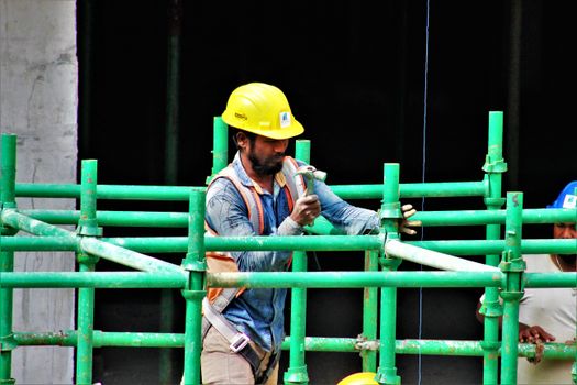 A construction worker using a hammer to assemble green scaffolding on a building site.