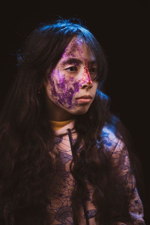 Free A young girl with colorful glitter face paint, captured in a moody and artistic portrait. Stock Photo
