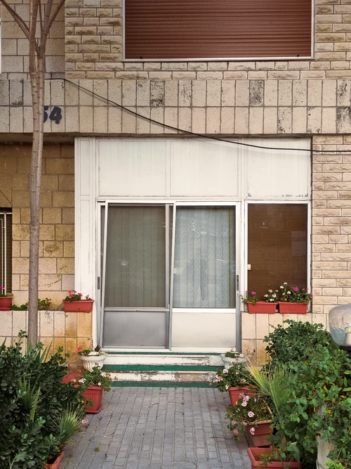 Free Front view of a residential entrance surrounded by greenery and flower pots, ideal for urban living themes. Stock Photo