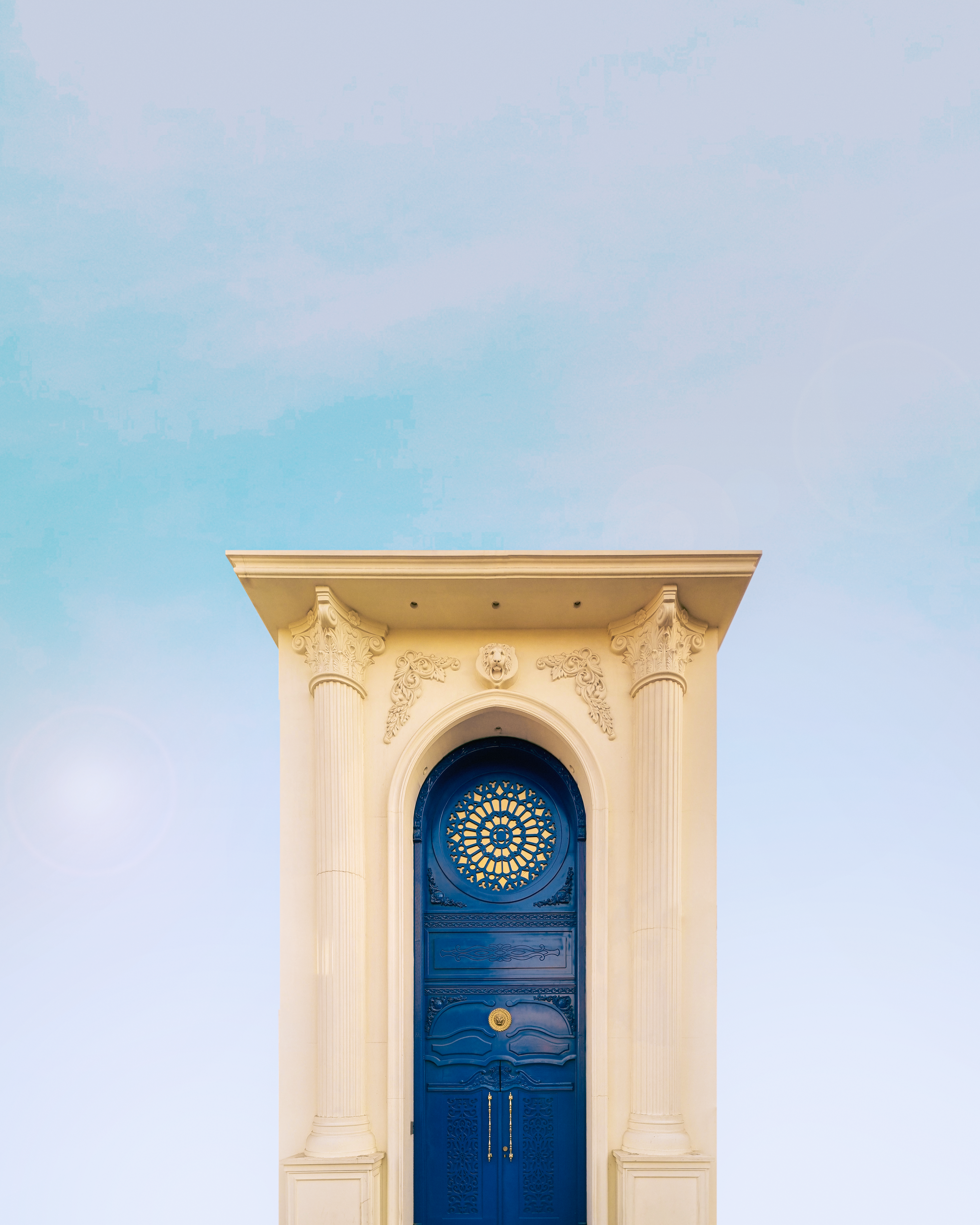 Elegant architectural detail featuring a blue door with intricate columns and arch against the sky.