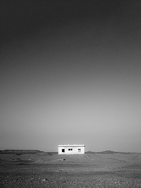 A solitary hut in a barren desert landscape with clear skies above.