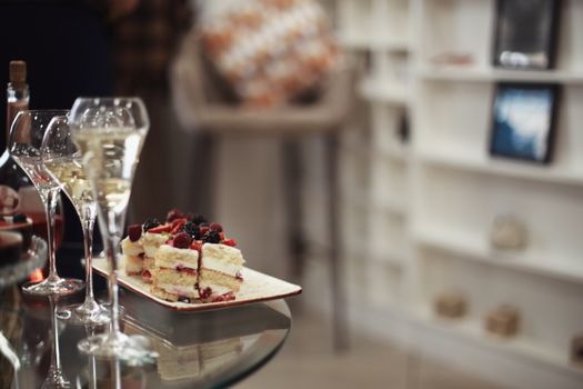 A slice of berry cake with wine glasses in a cozy indoor dining ambiance.