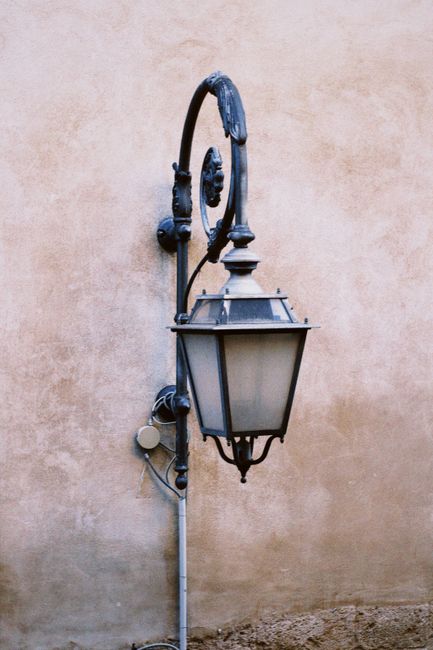 Classic wrought iron lantern on an aged plaster wall in a city setting.