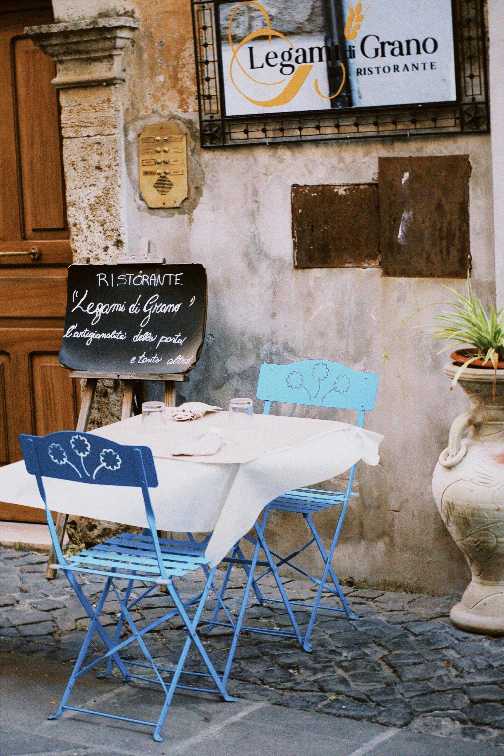 Quaint outdoor dining setup at a rustic Italian bistro with blue chairs and signage.