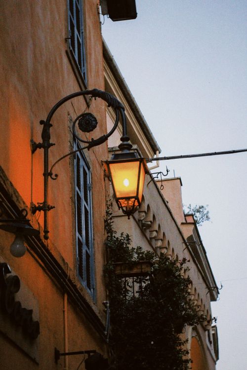 Free Vintage lantern illuminating an old street corner with warm glow and rustic building facade. Stock Photo