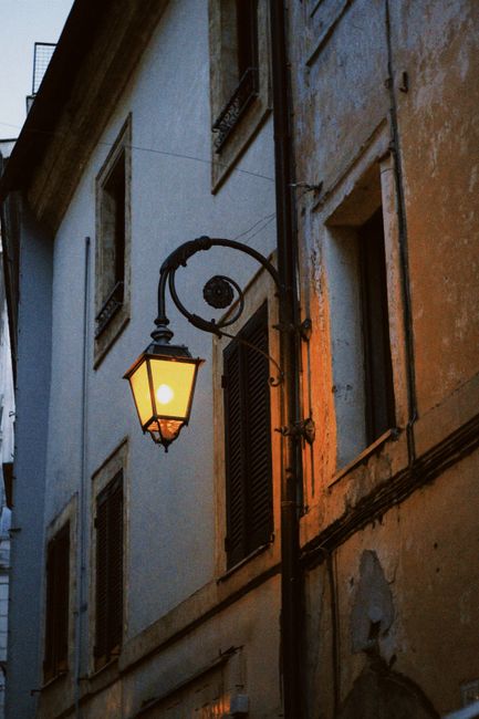 A vintage street lantern shines warmly in a historic alleyway, evoking classic European charm.