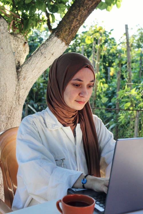 Free Young Woman Sitting at the Table and Using a Laptop  Stock Photo