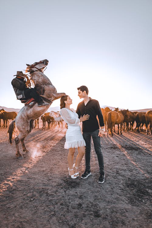 Couple Standing against Horse on Ends with Riders and Herd of Horses