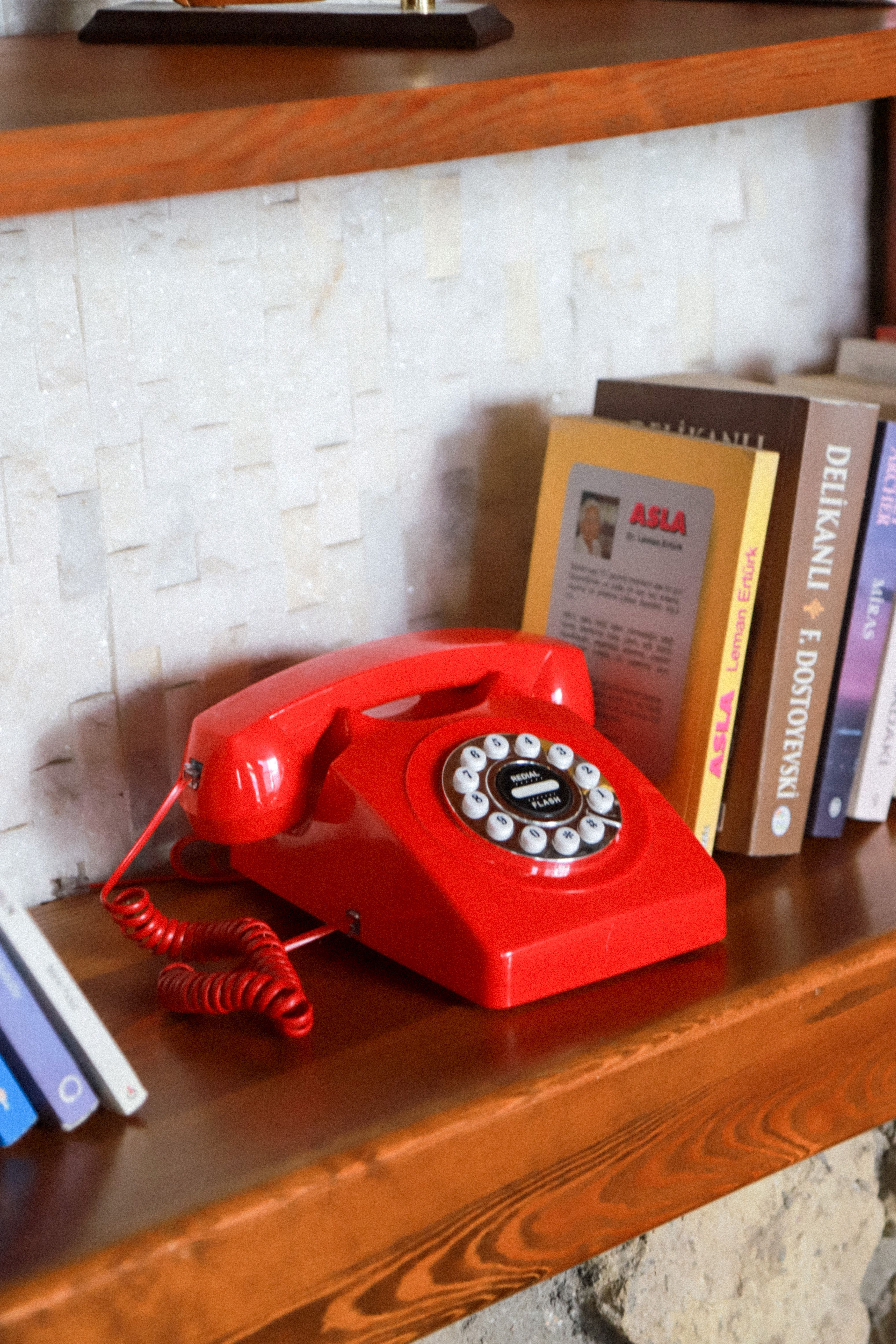 A classic red rotary dial phone sits on a bookshelf, evoking retro vibes.