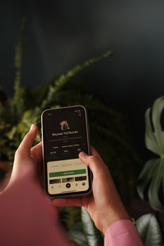 Close-up of hands holding a smartphone with app interface amidst green plants.