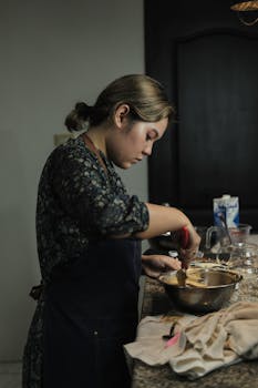 An adult woman in an apron mixing ingredients in a bowl, focused on her cooking.