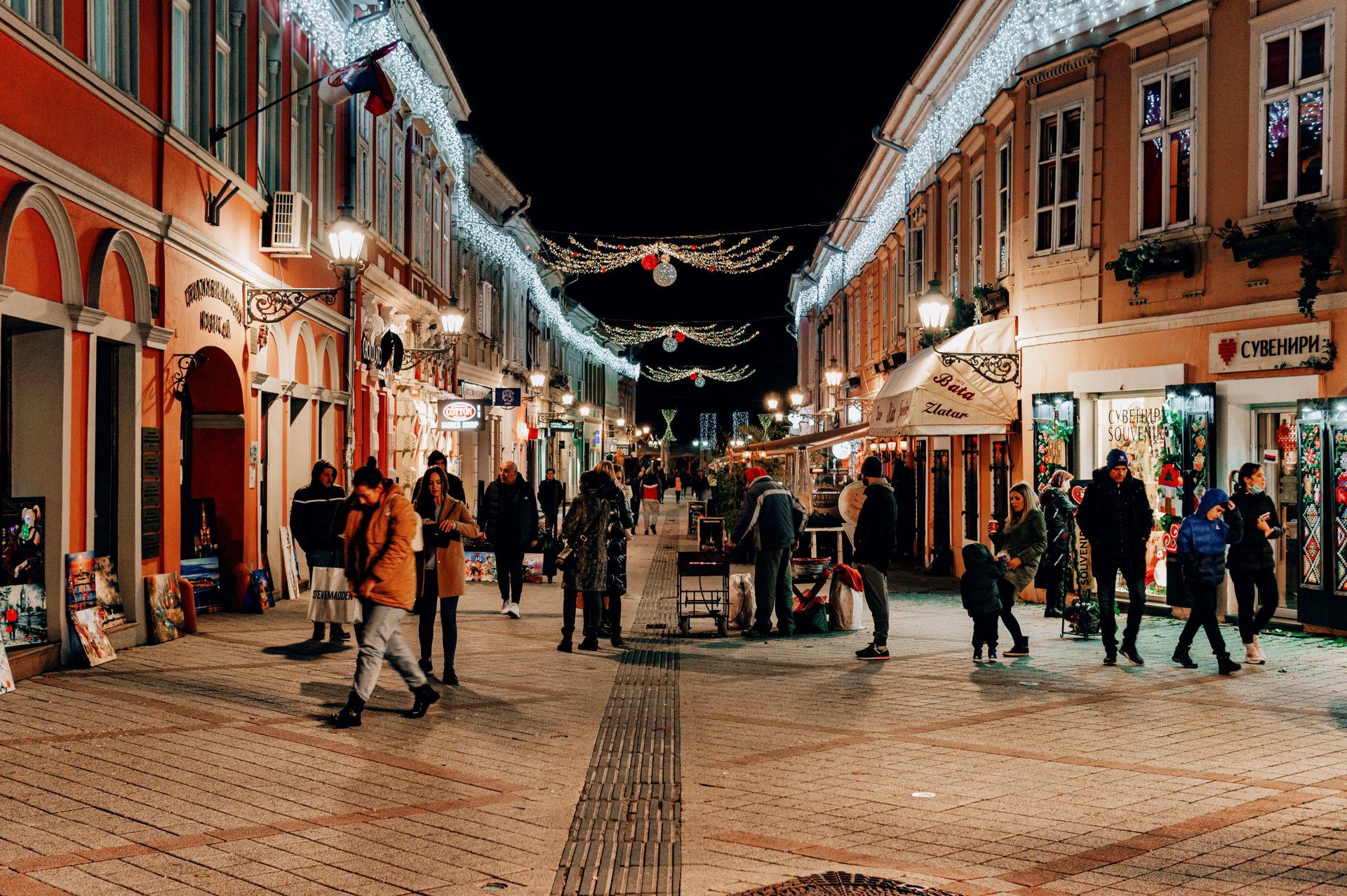 Lively pedestrian street in Novi Sad with festive lights and people at night.