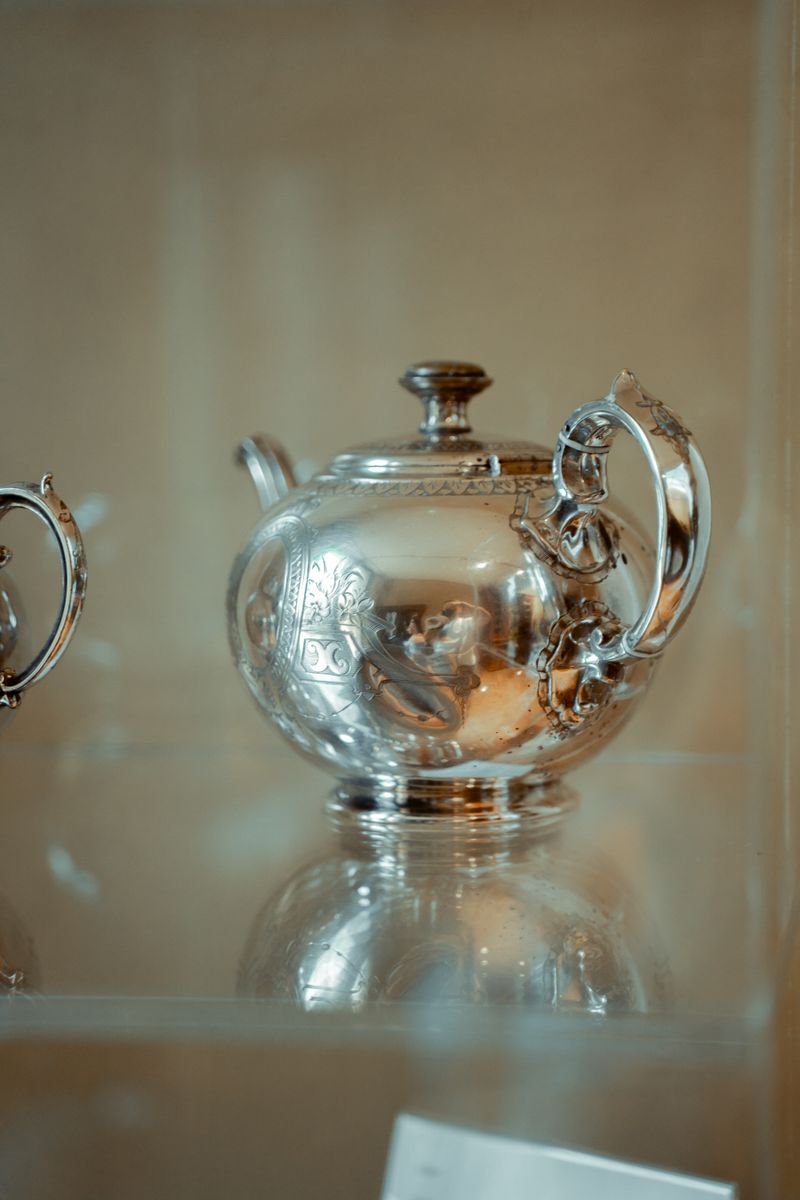 Ornate antique silver teapot with figural handle in a glass museum display case