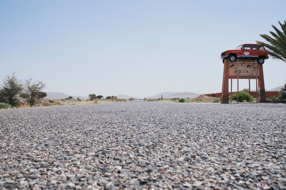 A scenic desert roadside view with a vintage car mounted on a display in Morocco.