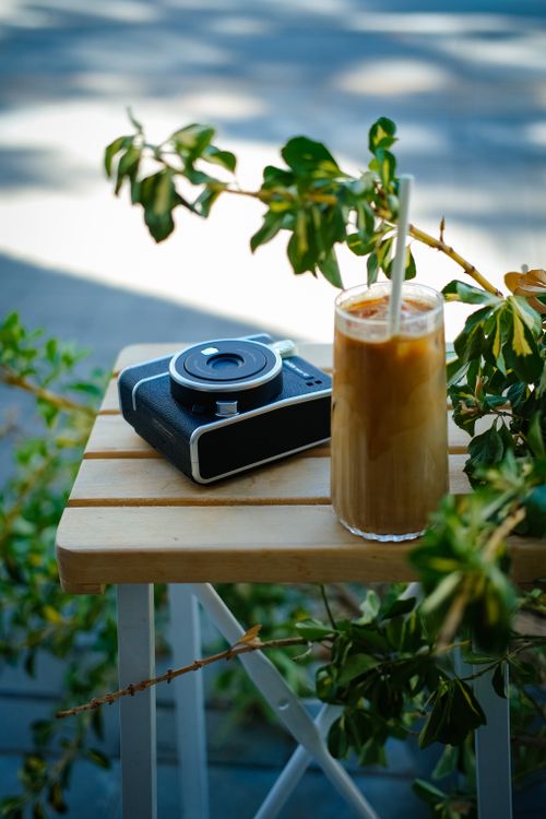 Free A refreshing iced coffee and vintage camera on a wooden table surrounded by greenery in Ankara, Türkiye. Stock Photo