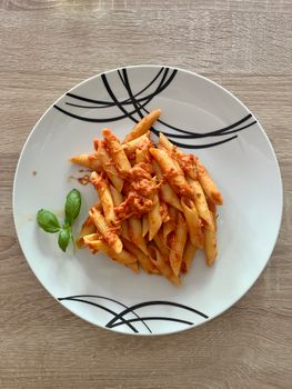 A top-down view of penne pasta with tomato sauce, garnished with basil, served on a white plate.