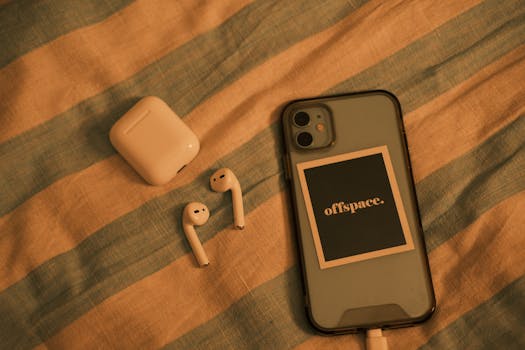 Close-up view of a smartphone and wireless earbuds on a striped fabric background.
