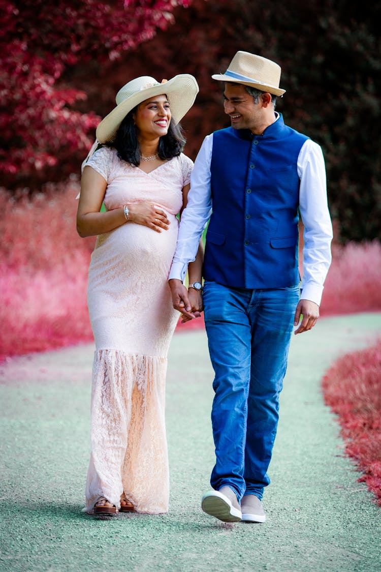 A Pregnant Woman And Her Partner Walking Together And Smiling 