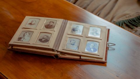 A vintage photo album lies open on a classic wooden table with a cozy fabric curtain backdrop.