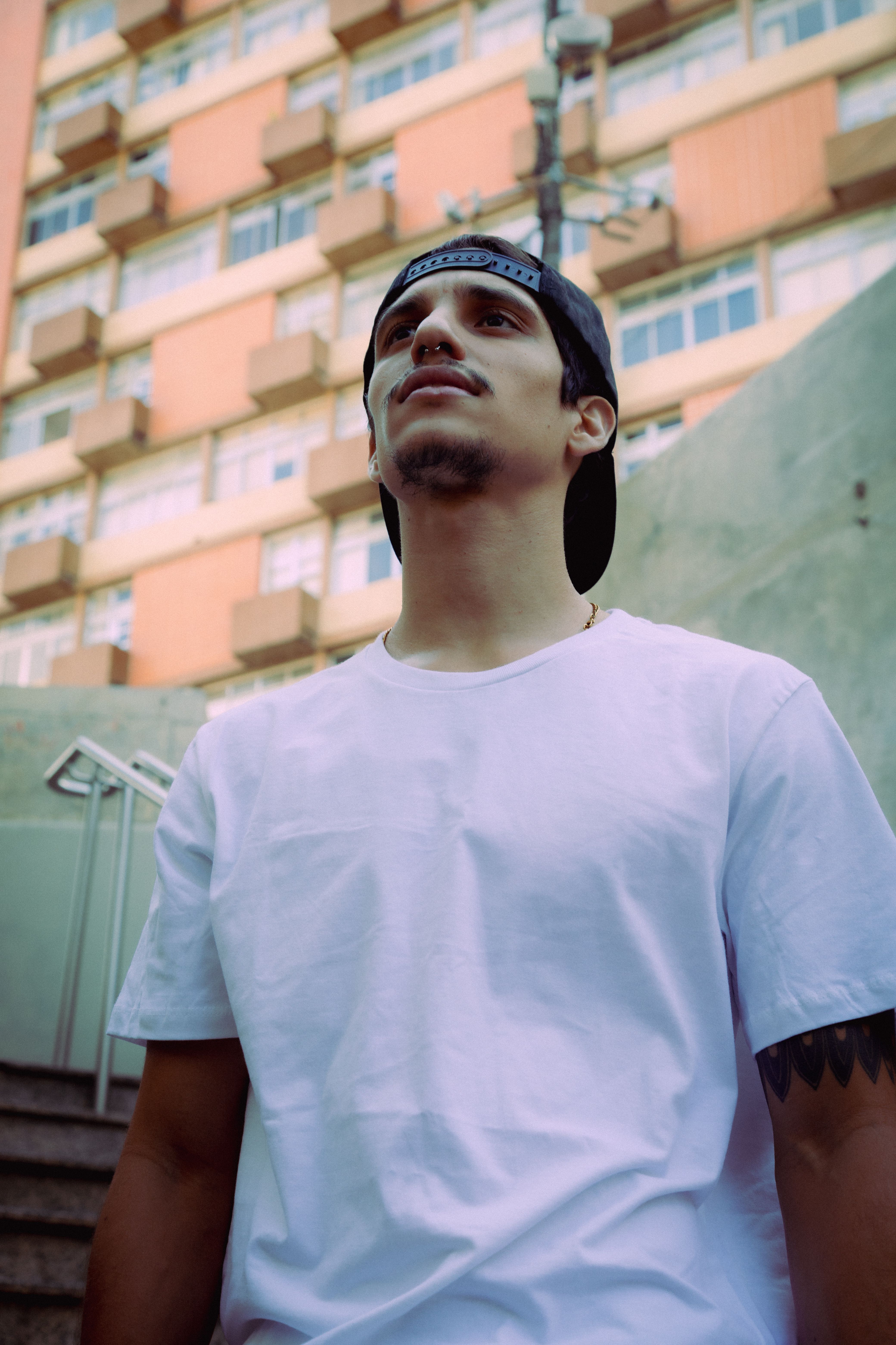 A young man in a white t-shirt and cap stands in front of a São Paulo apartment block.